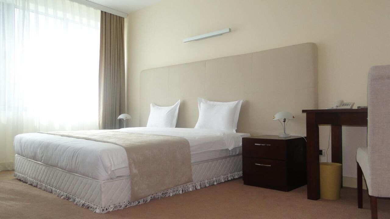 A hotel room with a large bed, a bedside table, a chair, and a desk.