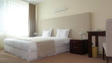 A hotel room with a large bed, a bedside table, a chair, and a desk.