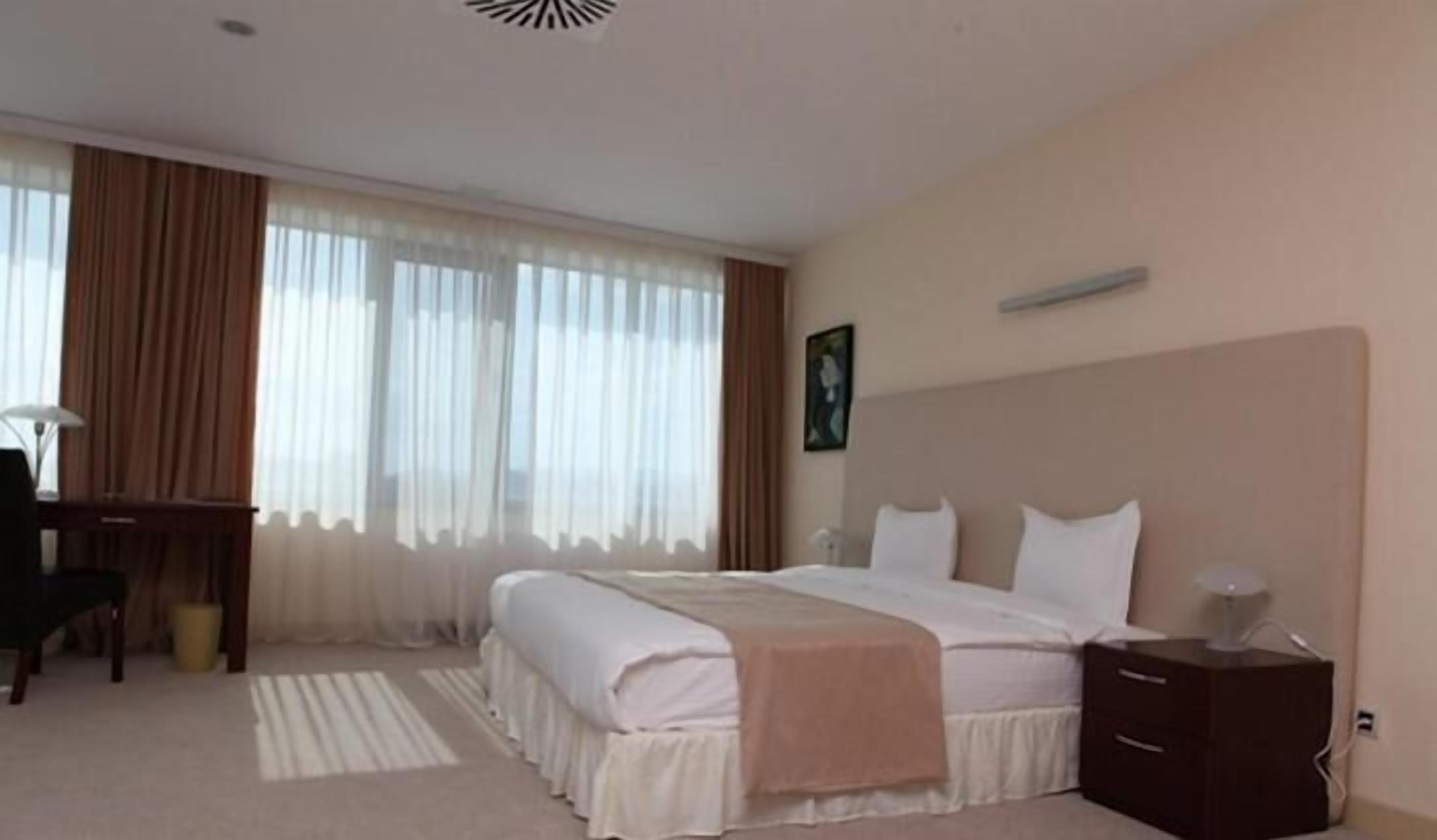 A hotel room with a large bed, a desk, a chair, and a bedside table.