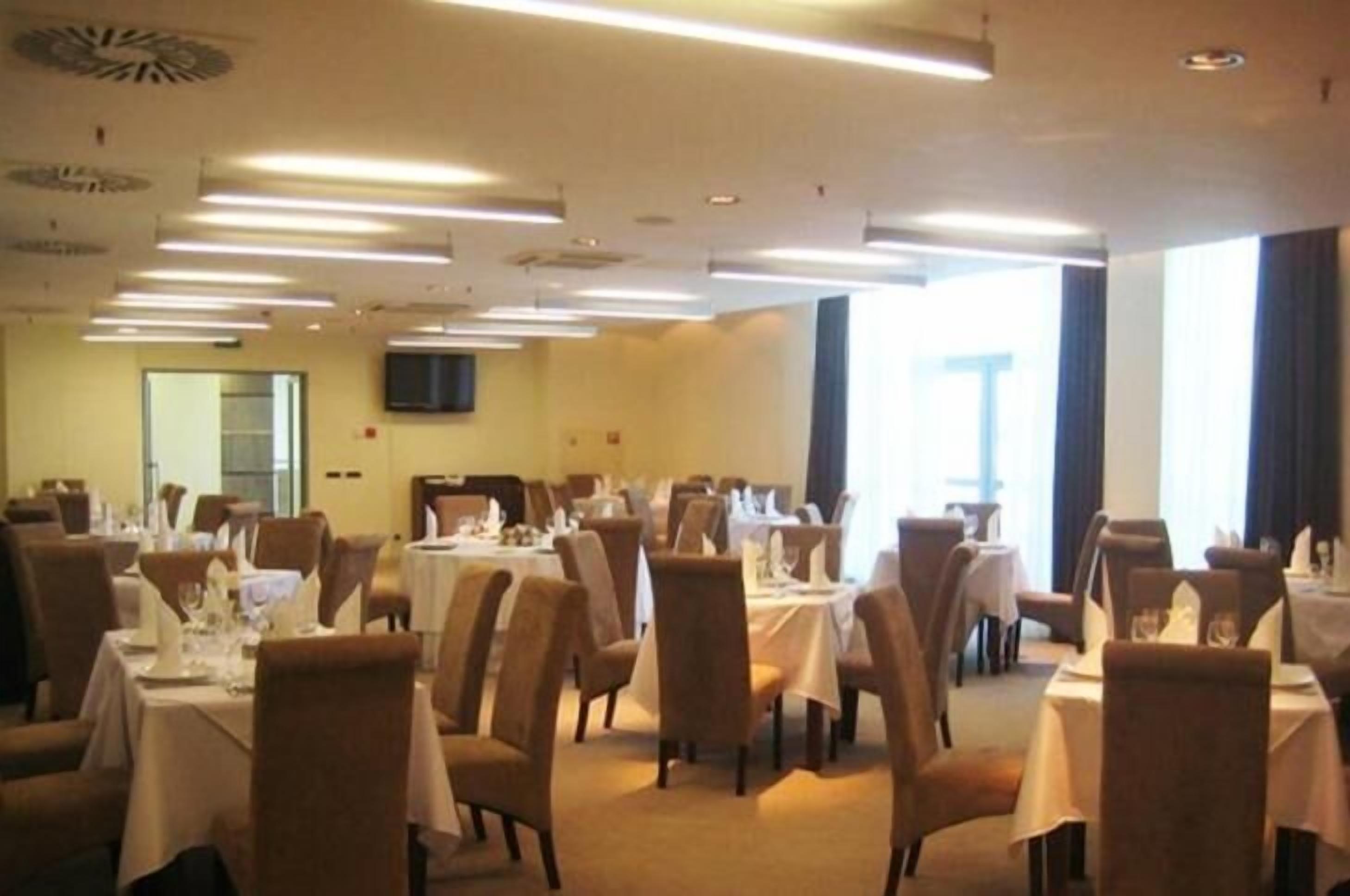 A conference room with multiple tables and chairs, equipped with overhead lighting and a television screen on the wall.