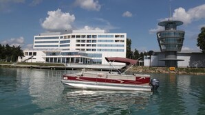 A boat docked near a modern building with a tower, a marina, and a clear sky. - Arena Hotel Kur (Mingacevir)