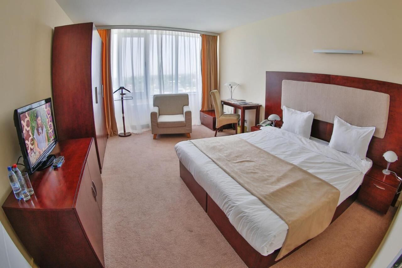 Quarto de hotel com uma cama grande, uma escrivaninha com cadeira, televisão e vista para o exterior pela janela.