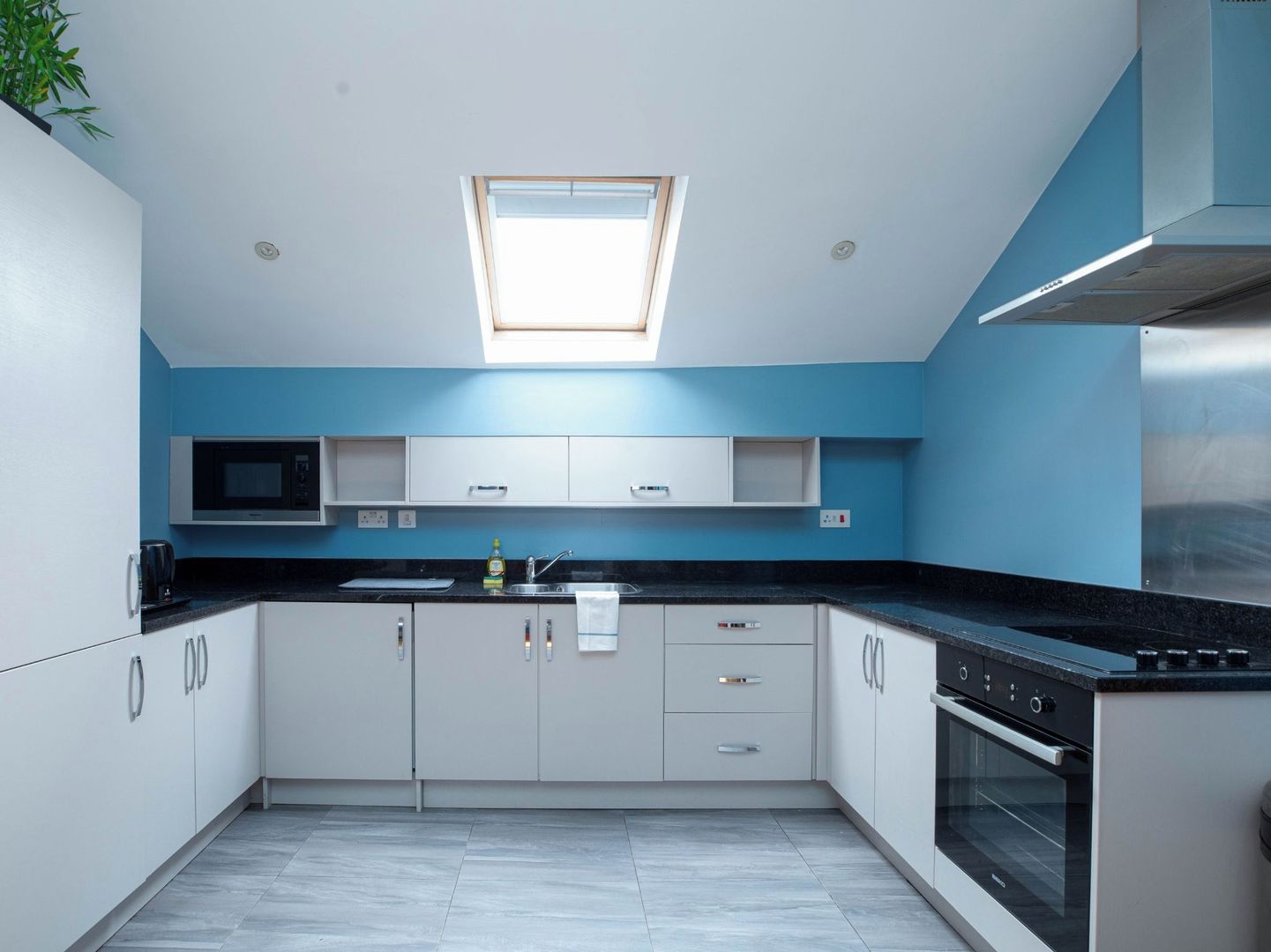 A modern kitchen with white cabinets, a black countertop, a microwave, a sink, and an oven.