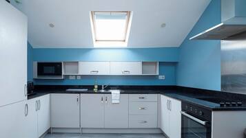 A modern kitchen with white cabinets, a black countertop, a microwave, a sink, and an oven.