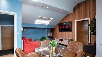 Una sala de estar moderna con sofás de cuero, una mesa de centro de vidrio y un televisor montado que muestra 'NETFLIX'.