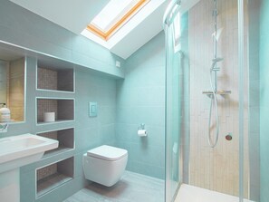 Un baño moderno con tragaluz, ducha con cerramiento de vidrio y un inodoro blanco.