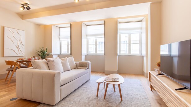 Una sala de estar moderna con un sofá, una mesa de centro, un televisor y ventanas amplias.