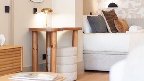 Un dormitorio moderno con una mesita de noche de madera, una lámpara redonda, un sofá con cojines estampados y un cajón auxiliar.