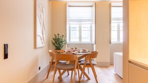 Un comedor con una mesa dispuesta para cuatro, sillas de madera, una planta en maceta y una ventana con persianas.