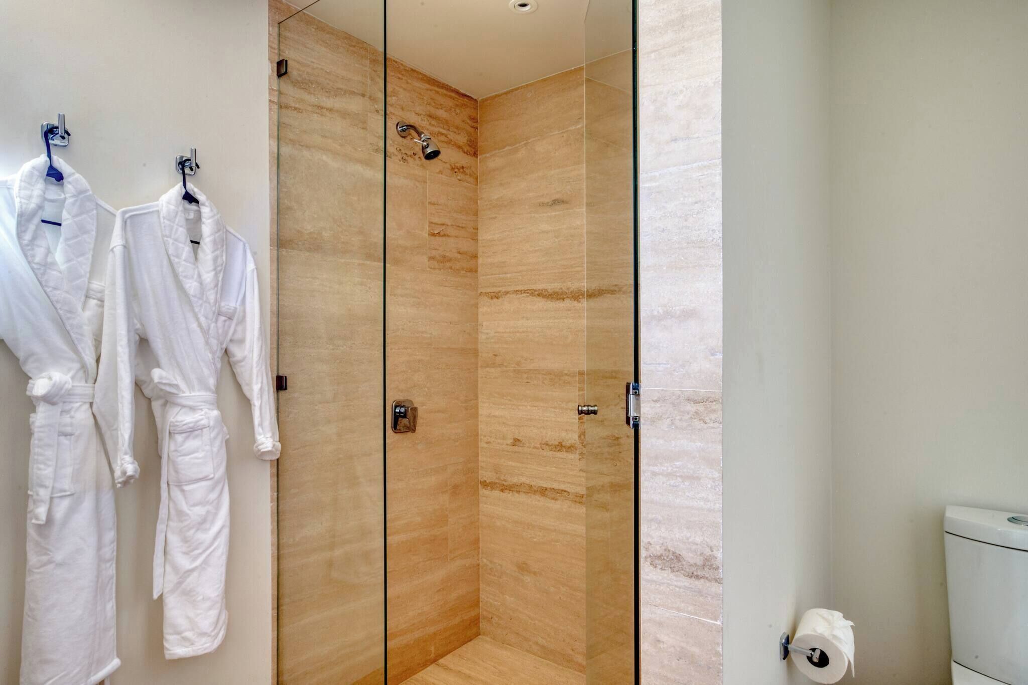 A modern bathroom with a glass-enclosed shower, white towels, and a toilet.