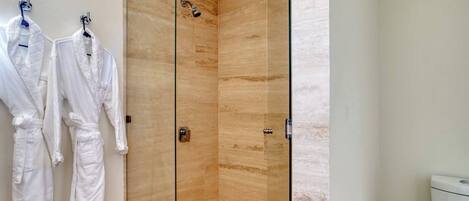 A modern bathroom with a glass-enclosed shower, white towels, and a toilet.