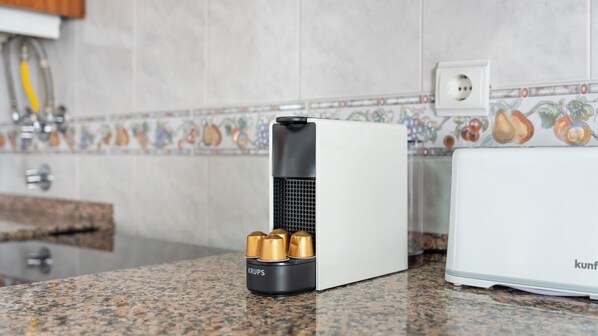 A kitchen with a white appliance, a black and gold device, and a tiled backsplash.
