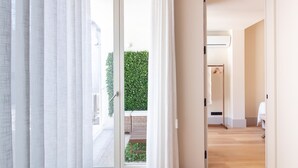 Un interior moderno con suelo de madera, vistas a un seto verde exterior y una puerta blanca que conduce a otra habitación.