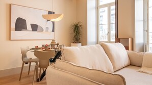 A modern living room with a sofa, a dining table with chairs, a potted plant, and a large window. - Catarina 392 | Chic Studio by LovelyStay (Porto)