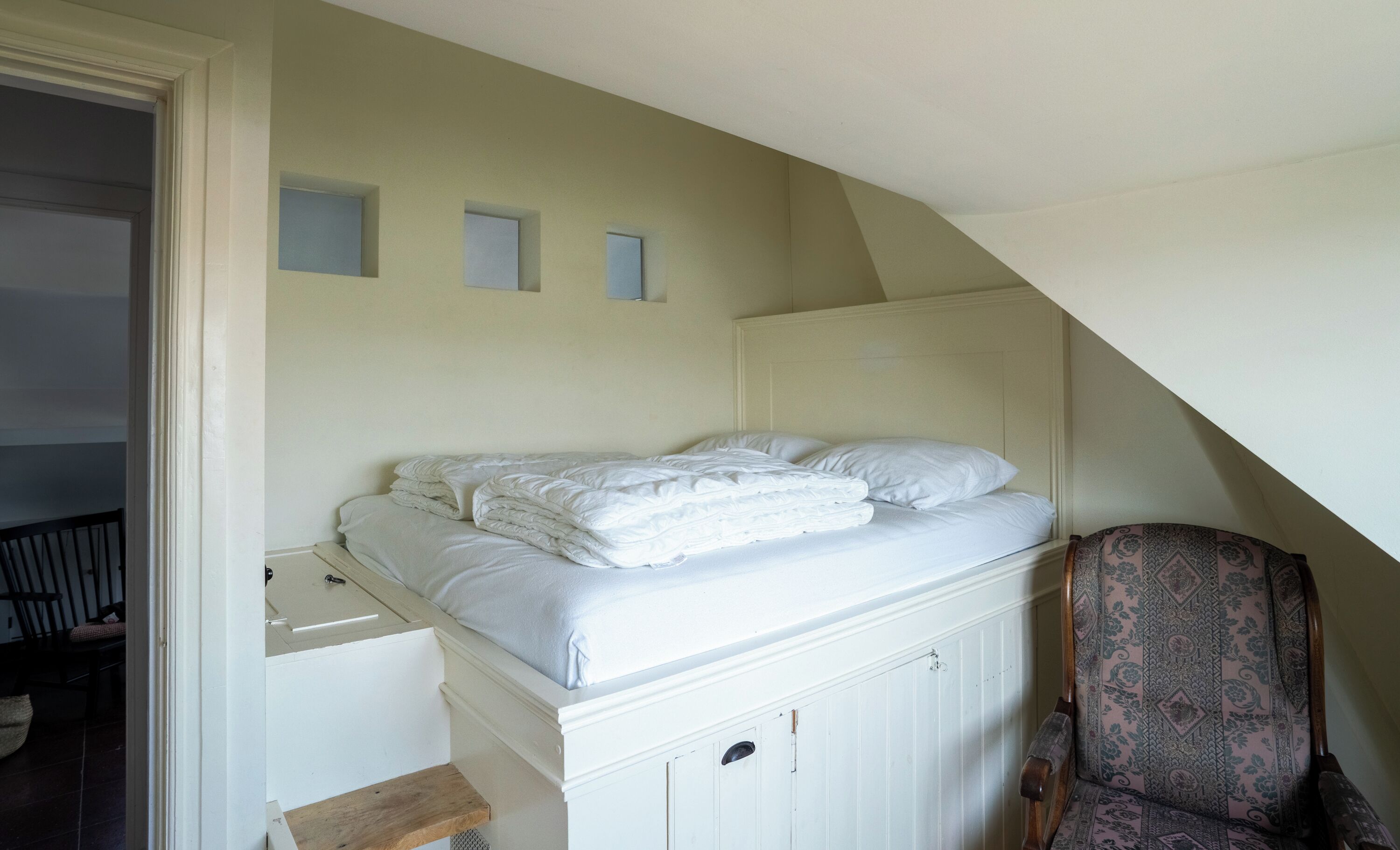 A bedroom with a bed, a chair, and a wardrobe.