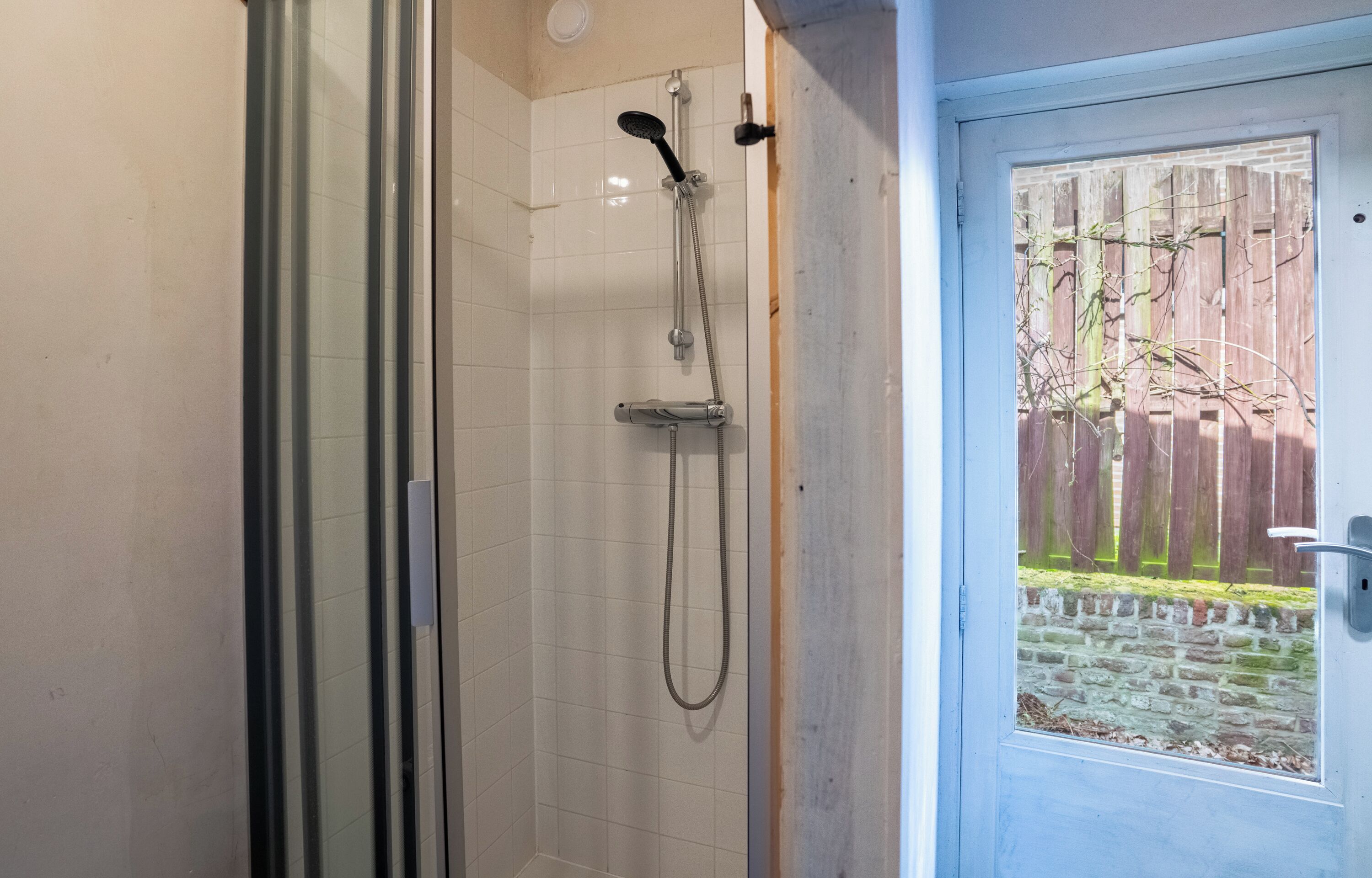 Een douche met een glazen deur, een metalen hendel en een douchetuit.