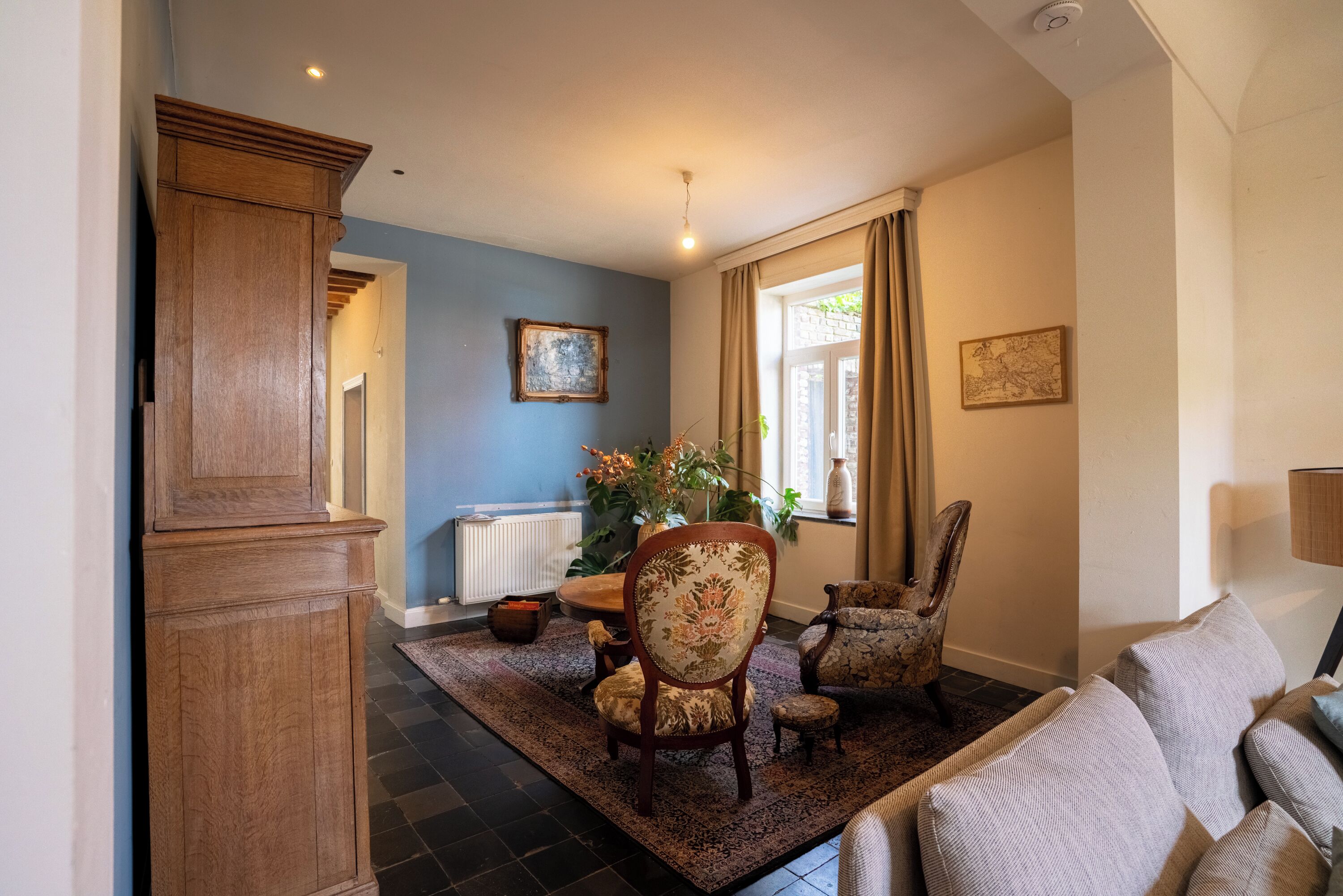 Una sala de estar con un mueble de madera grande, un sillón floral, un sillón estampado, un sofá y una mesa de centro.