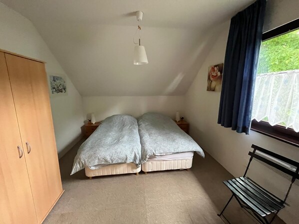 Un dormitorio con cama, armario de madera, banco, ventana con cortinas y una lámpara colgante.