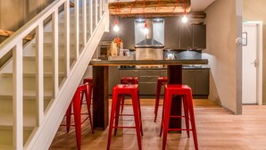 Una cocina moderna con una isla central, taburetes rojos y una escalera con barandas blancas.