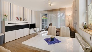 A modern living room with a white sofa, a dining table, and a kitchen area with a TV and cabinets.