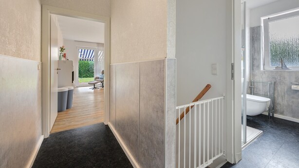 A hallway with a wooden floor, a white railing, and a view into a room with a bathtub.