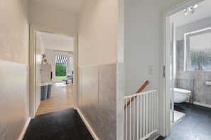A hallway with a wooden floor, a white railing, and a view into a room with a bathtub.