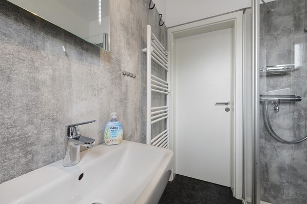 A bathroom with a white sink, a bottle of hand soap, a towel rack, and a glass shower enclosure.