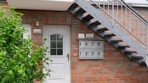 A brick building with a white door, a mailbox with numbers, and a metal staircase.