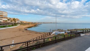 Vista costeira com uma praia de areia, um calçadão de madeira e um edifício com vários andares ao fundo.