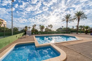Une piscine dont le fond est recouvert de motifs géométriques en mosaïque, entourée de palmiers et surplombée d’un ciel dégagé.