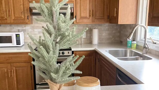 A kitchen with wooden cabinets, a microwave, a sink, and a decorative tree on the counter.