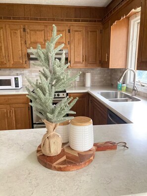 A kitchen with wooden cabinets, a microwave, a sink, and a decorative tree on the counter.