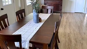 A dining room with a wooden table, chairs, a vase with plants, and a cabinet with decorative items.