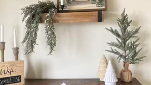 A wooden desk with a framed picture of a barn, a small Christmas tree, and a candle holder with greenery.