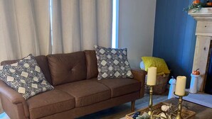 A brown leather sofa with patterned cushions, a wooden coffee table with candles and decorative items, and a patterned rug.