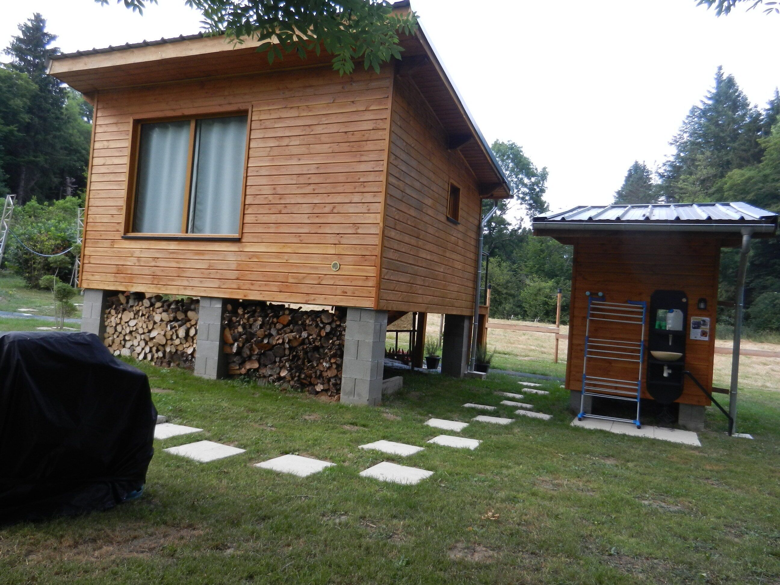Eine Holzhütte mit kleinem Anbau-Badezimmer und überdachter Grillgelegenheit.