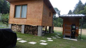 Eine Holzhütte mit kleinem Anbau-Badezimmer und überdachter Grillgelegenheit.