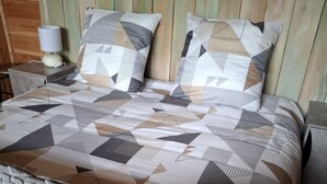 Una cama con una colcha de estampado geométrico, dos almohadas con diseños geométricos y una almohada decorativa con texto.