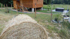 Una cabaña de madera con una escalera que sube a un dormitorio en el altillo, rodeada de césped y árboles.