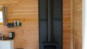 Una habitación acogedora con paredes de madera, una estufa de leña negra, una pequeña cocina con un hervidor y un taburete.