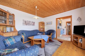 A cozy living room with a wooden ceiling, a blue sofa set, a wooden coffee table, and a television on a wooden stand. - Holiday Home 'Von Bargen' with Private Terrace, Garden, and Wi-Fi (Cuxhaven)