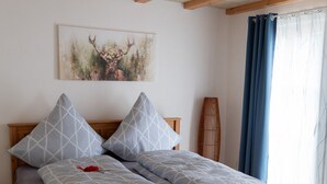 A wooden bed with a grey and white patterned bedspread, two pillows, a red object on the bed, and a painting on the wall.