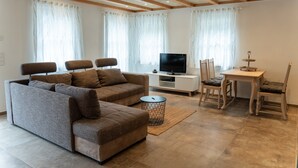 A modern living room with a sectional sofa, a TV, a dining table with chairs, and a small side table.