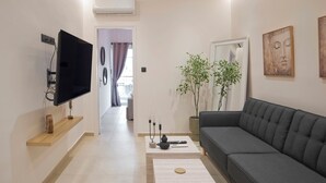 Een moderne woonkamer met een flatscreen televisie, een grijze bank, een plant in pot en kunstwerken aan de wanden.