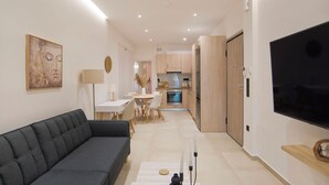 Een moderne woonkamer met een bank, een eettafel en een keukenhoek met kasten en een televisie.