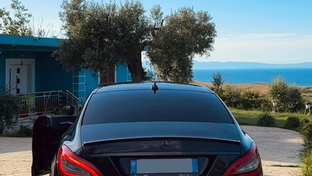 A black car parked on a paved driveway with a clear blue sky and distant mountains in the background.