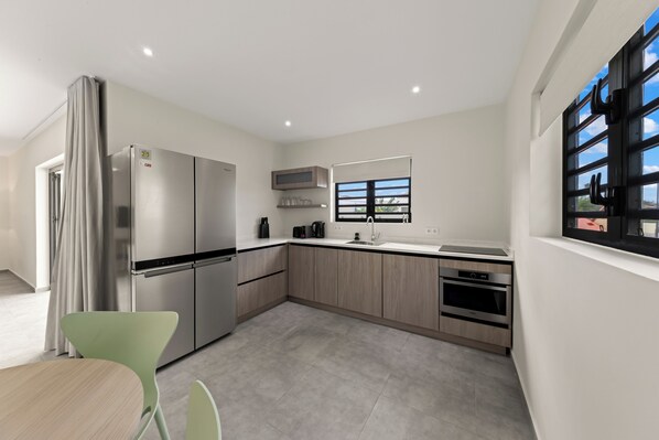 A modern kitchen with stainless steel appliances, light wood cabinets, and a window with a view. - Apartment Serena, Mambo Beach (Willemstad)