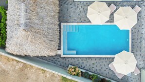 Area piscina sul tetto con una piscina azzurra, ombrelloni bianchi e una poltrona da relax con tetto di paglia.