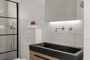 Een moderne badkamer met een rechthoekig wastafelmeubel, een douchecabine van glas en een handdoekrek met bloemen.