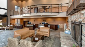 A spacious lobby with a curved balcony, leather sofas, a reception desk, and a stone fireplace.